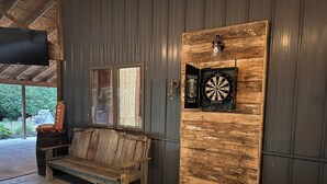 A rustic interior with a wooden bench, a dartboard, and a window with patterned curtains.