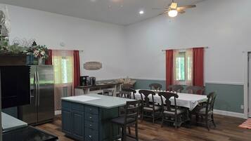 A spacious kitchen with a central island, wooden dining table, and chairs. There are ceiling fans and recessed lighting.