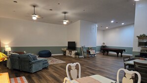 A spacious living room with a sofa, a dining table with chairs, a pool table, and ceiling fans.