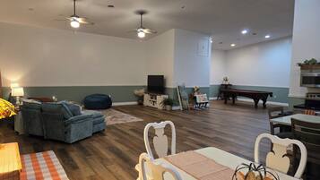 A spacious living room with a sofa, a dining table with chairs, a pool table, and ceiling fans.