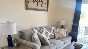 Ein Wohnzimmer mit grauem Sofa, zwei Beistelltischen, einem Couchtisch und einem an der Wand befestigten Schild.