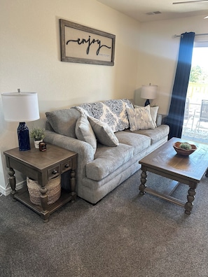 A living room with a grey sofa, two side tables, a coffee table, and a wall-mounted sign. - Beautiful Brand new! NO STAIRS Next to SDC! 2 king rooms queen sofa 2 full baths (Branson)