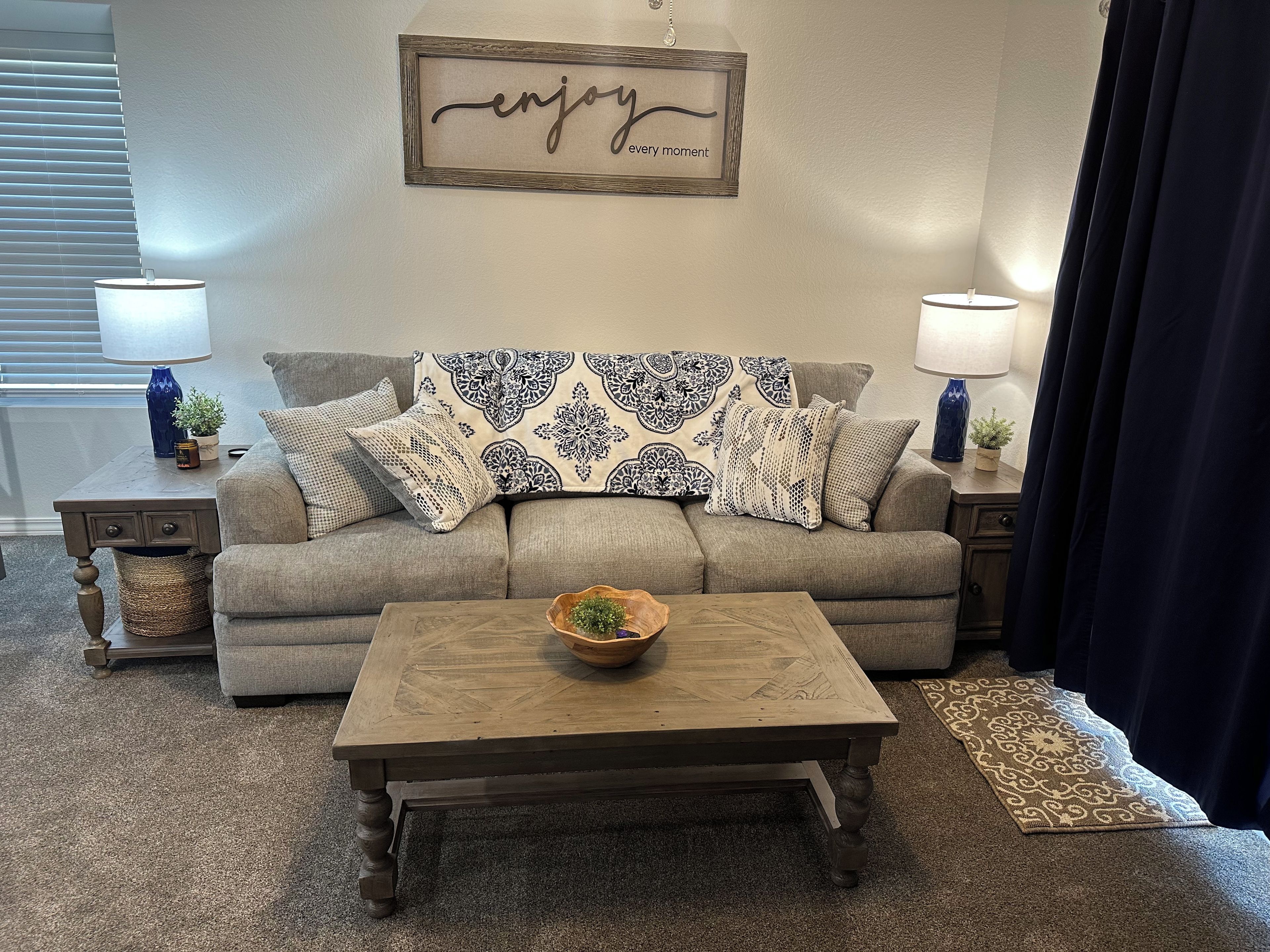 A living room with a sofa, two side tables, a coffee table, and a wall-mounted sign.