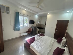 A hotel room with a bed, a desk, a chair, a television, and a door. - Rc Stays (Noida)
