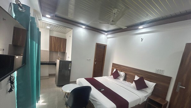 A hotel room with a bed, a desk, a chair, a wardrobe, and a kitchenette. - Rc Stays (Noida)