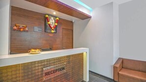 A reception area with a wooden reception desk, a framed picture above it, and a red carpet leading to a brown sofa. - Hotel Shreeyash Executive (Pune)