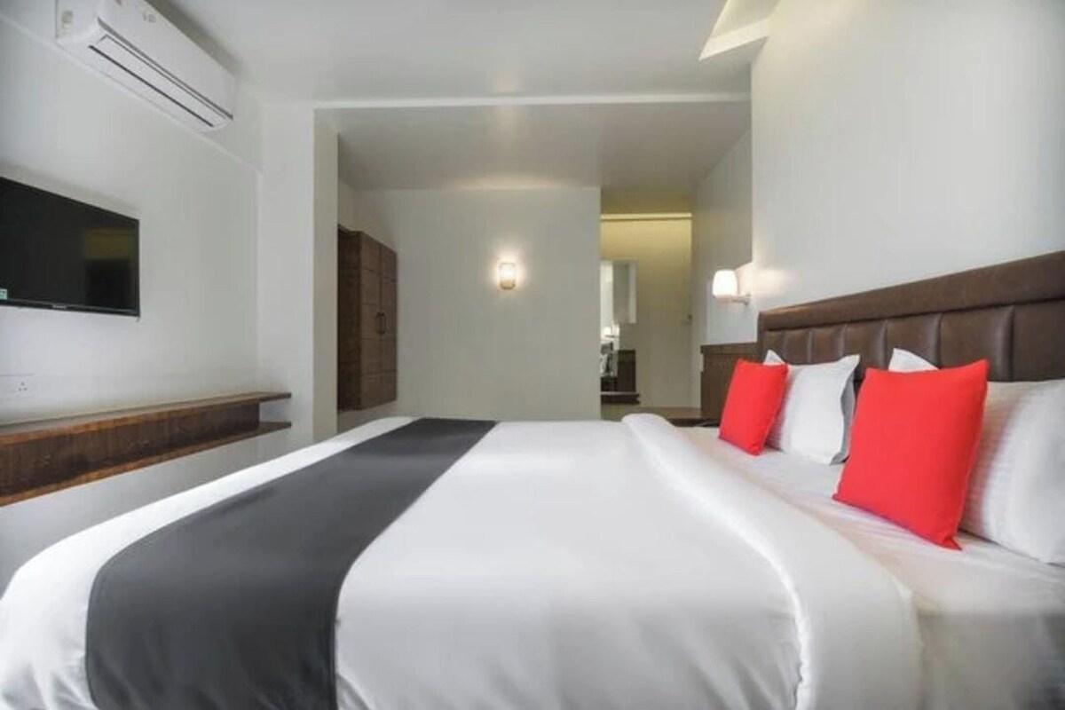 A hotel room with a large bed, a flat-screen TV mounted on the wall, and a wooden bench.