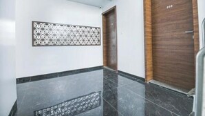 A hallway with a wooden door labeled "202", a decorative wall panel, and a black marble floor. - Hotel Shreeyash Executive (Pune)