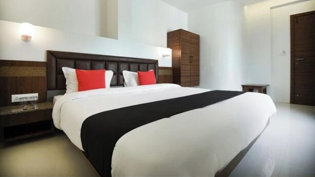 A modern hotel room with a large bed, a wooden headboard, a nightstand, a wardrobe, and a small table. - Hotel Shreeyash Executive (Pune)