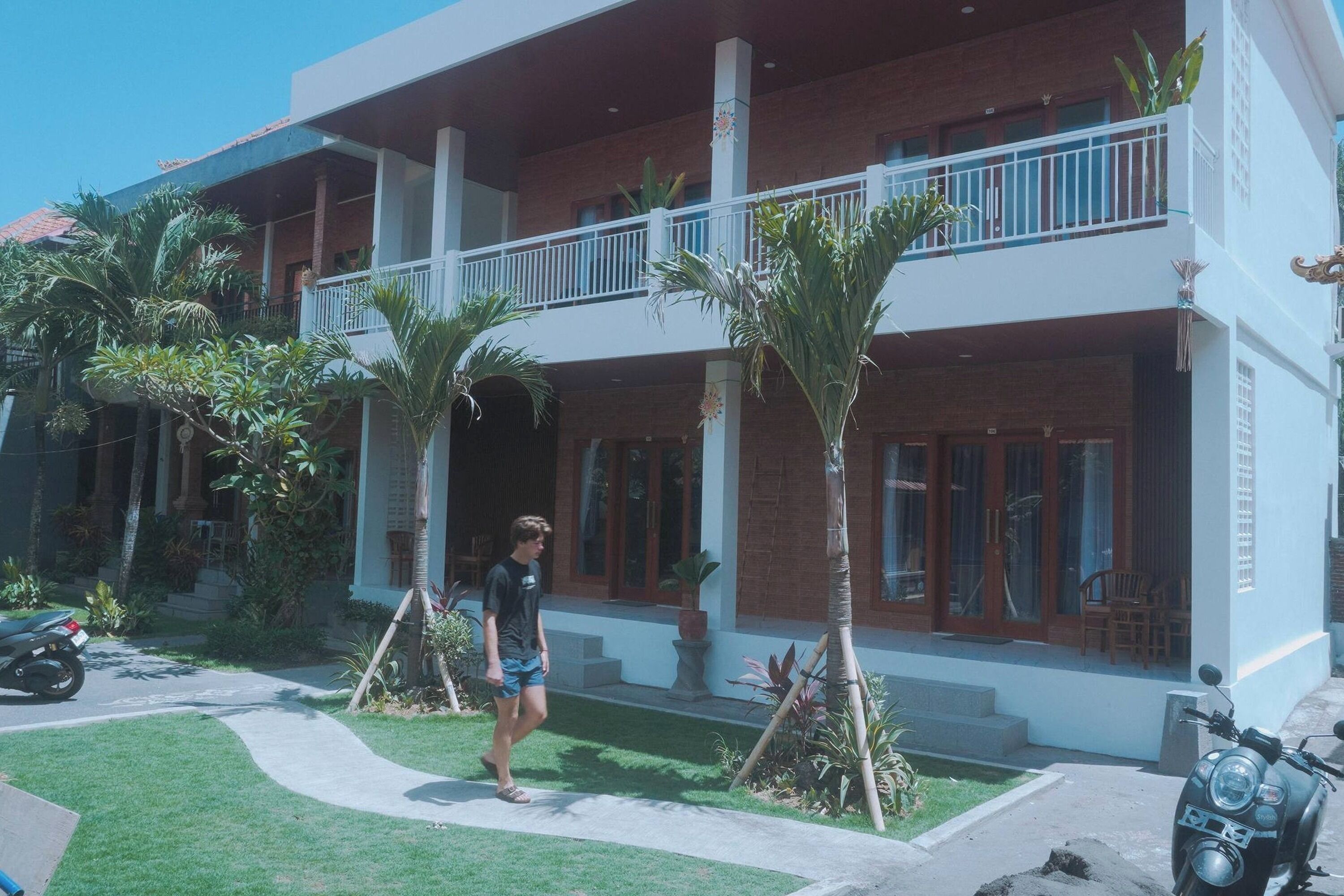 A two-story building with a balcony, a paved driveway, and a motorcycle parked in front.