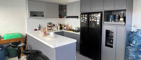 A modern kitchen with grey cabinets, a black refrigerator, a water dispenser, and a marble countertop.