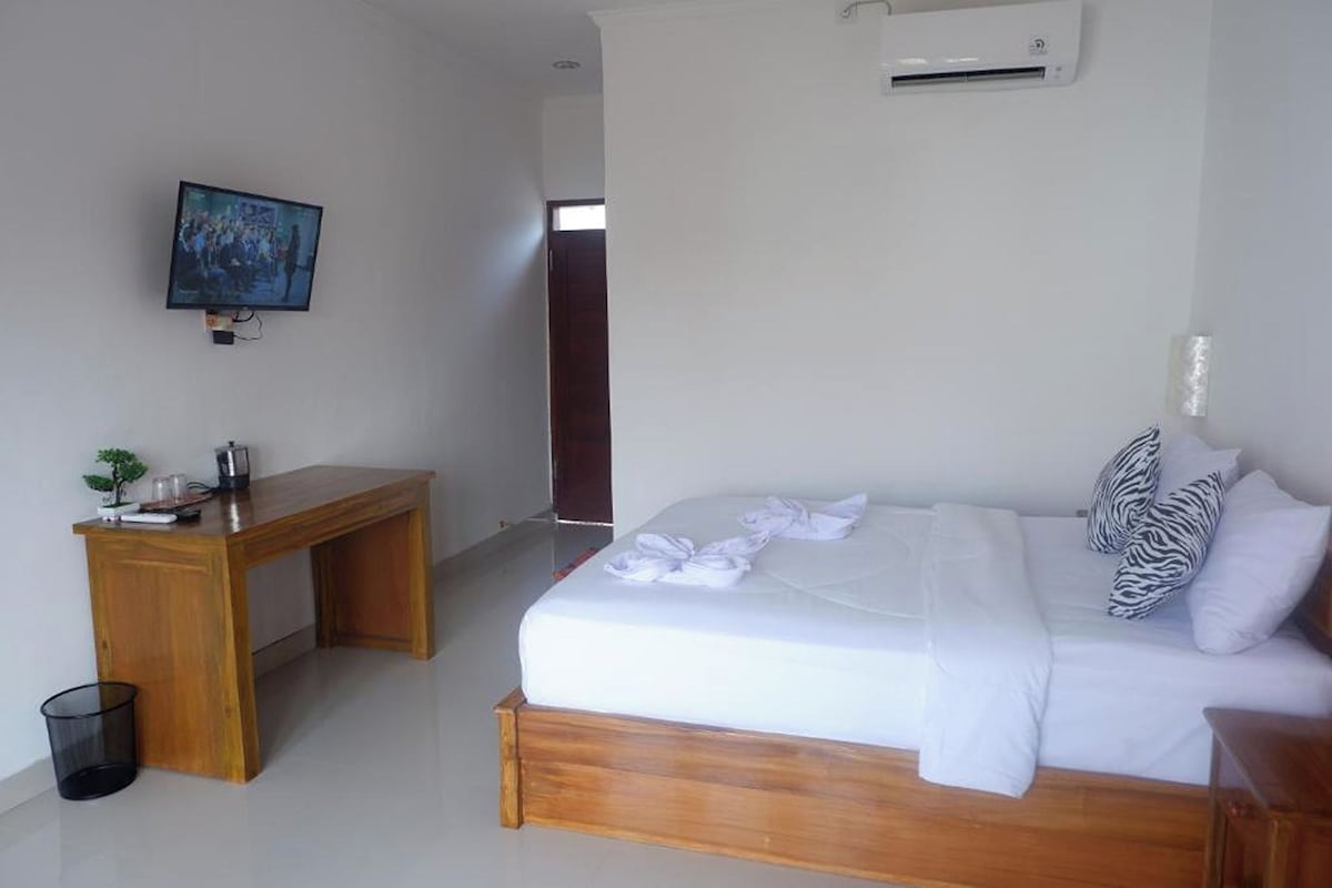 A bedroom with a bed, a desk, a TV, and an air conditioner.