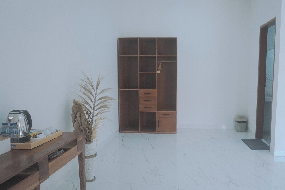 A room with a wooden wardrobe, a small table with a kettle, and a potted plant.