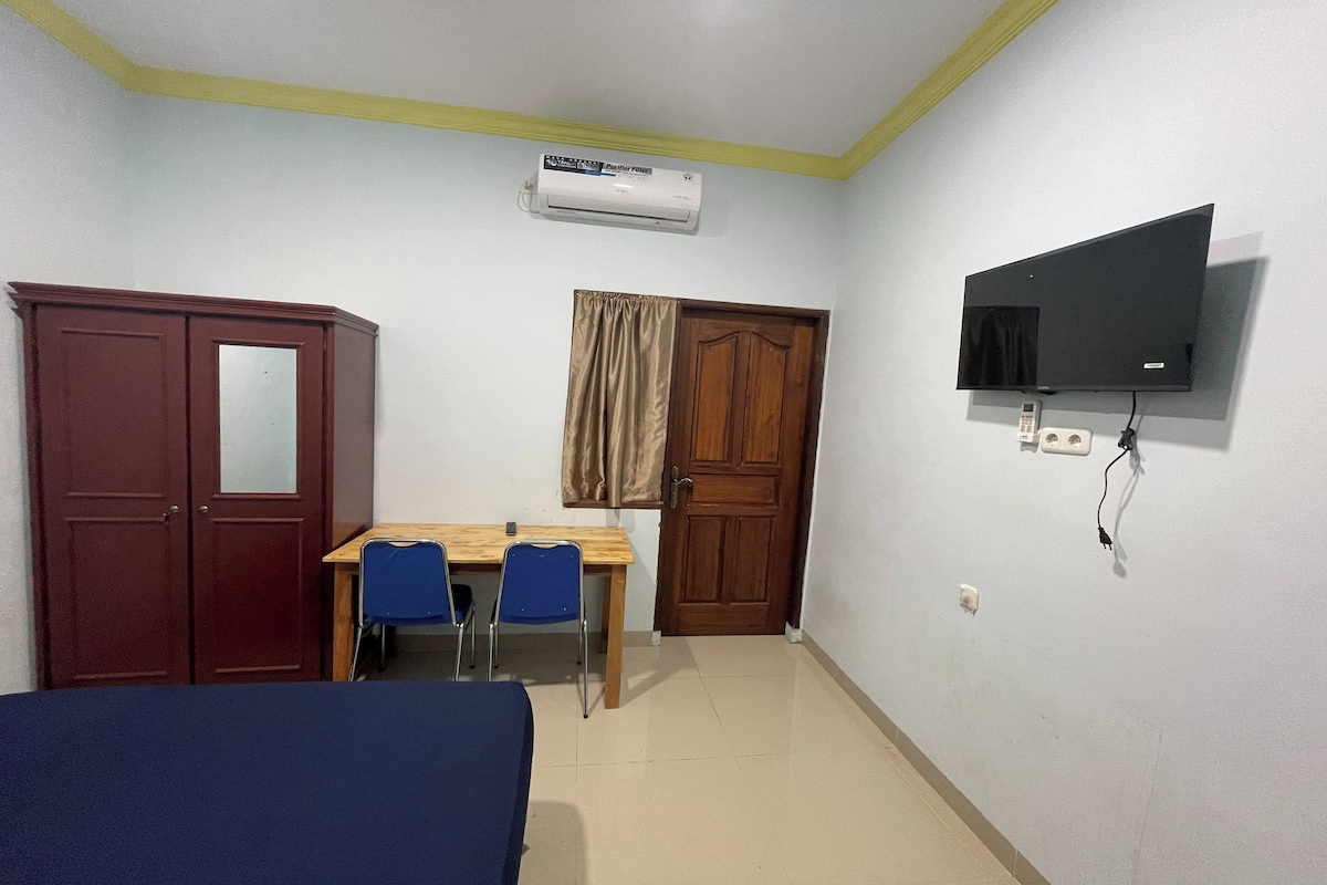 Une chambre comprenant un lit, un bureau avec deux chaises, une armoire, un téléviseur fixé au mur et un appareil de climatisation.