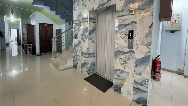 A hotel lobby with a marble wall, a staircase, and a fire extinguisher. - Blissful Executive Kost (Medan)