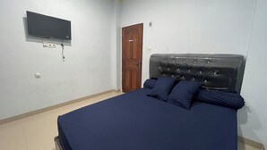 A bedroom with a bed, a wooden door, a television mounted on the wall, and a light switch. - Blissful Executive Kost (Medan)