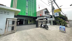 A building with a green facade, a gated entrance, and a motorcycle parked in front. - Blissful Executive Kost (Medan)