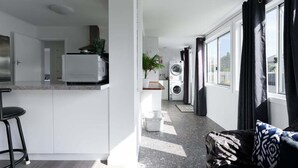 A modern kitchen with a built-in oven, a dining area with a bar stool, and a laundry area with a washing machine. - Modern Ease in East Devonport (City of Devonport)