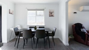 A dining area with a table and chairs, a window with blinds, and a potted plant. - Modern Ease in East Devonport (City of Devonport)