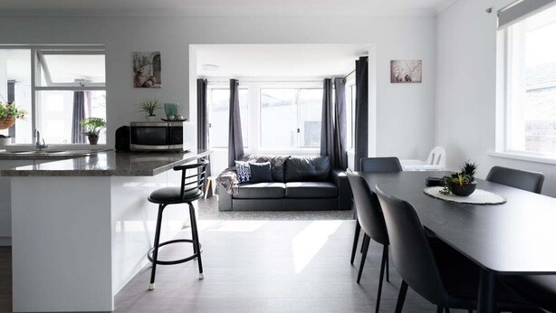 A modern kitchen with a central island, a dining area with a table and chairs, a sofa, and a TV. - Modern Ease in East Devonport (City of Devonport)