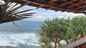 A wooden balcony with a view of the ocean and palm trees. - Griya Prasetaya (Wonosari)