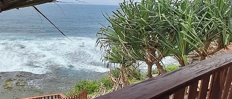 A wooden balcony with a view of the ocean and palm trees.
