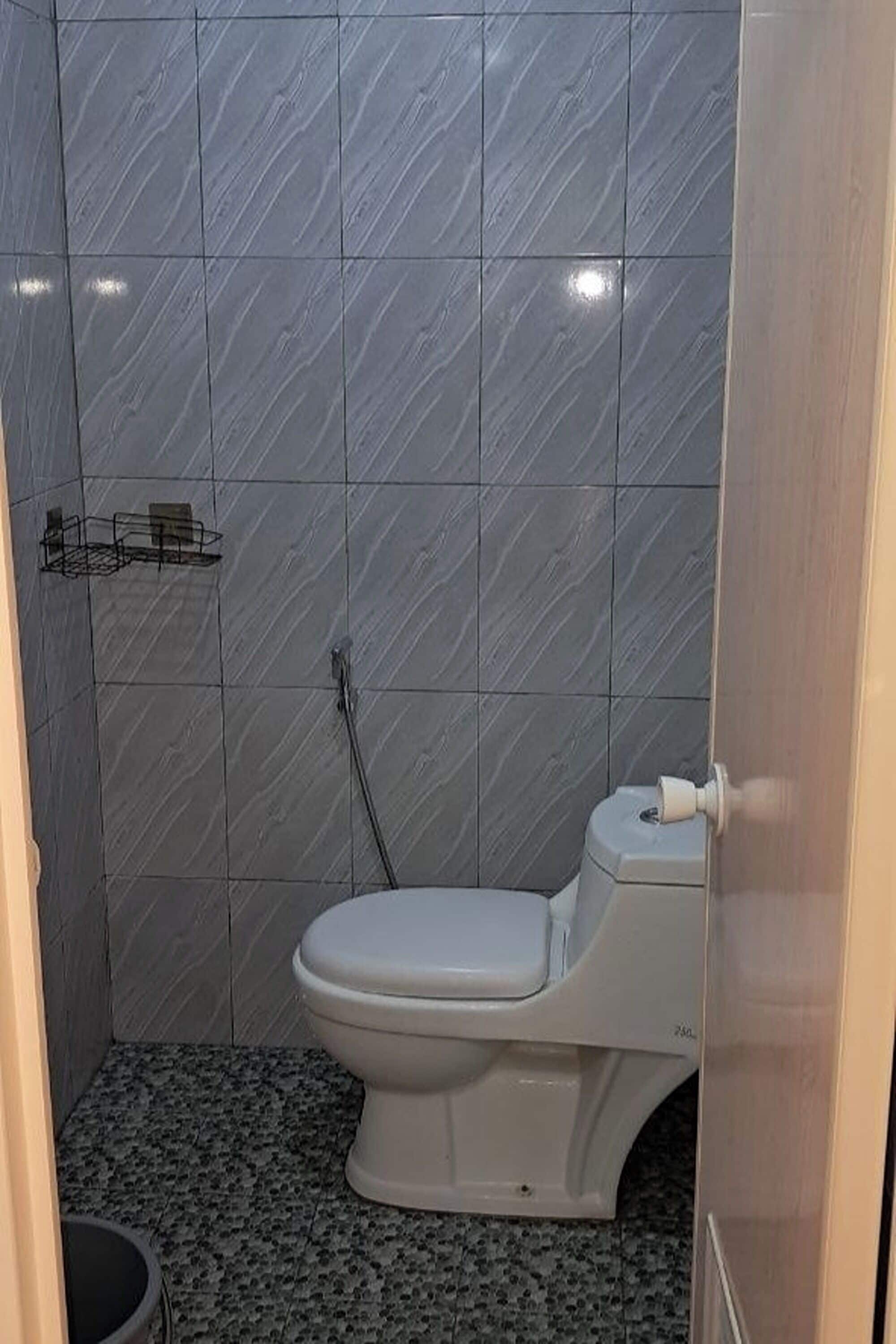 A small bathroom with a toilet, a metal rack, and a tiled wall.