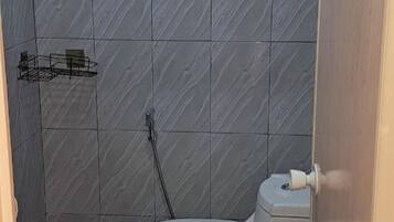 A small bathroom with a toilet, a metal rack, and a tiled wall.