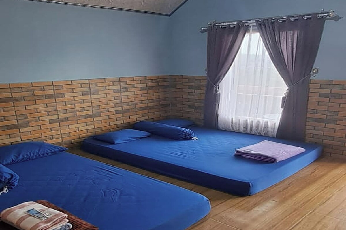 A room with two beds, a brick accent wall, a wooden floor, and a ceiling light fixture.