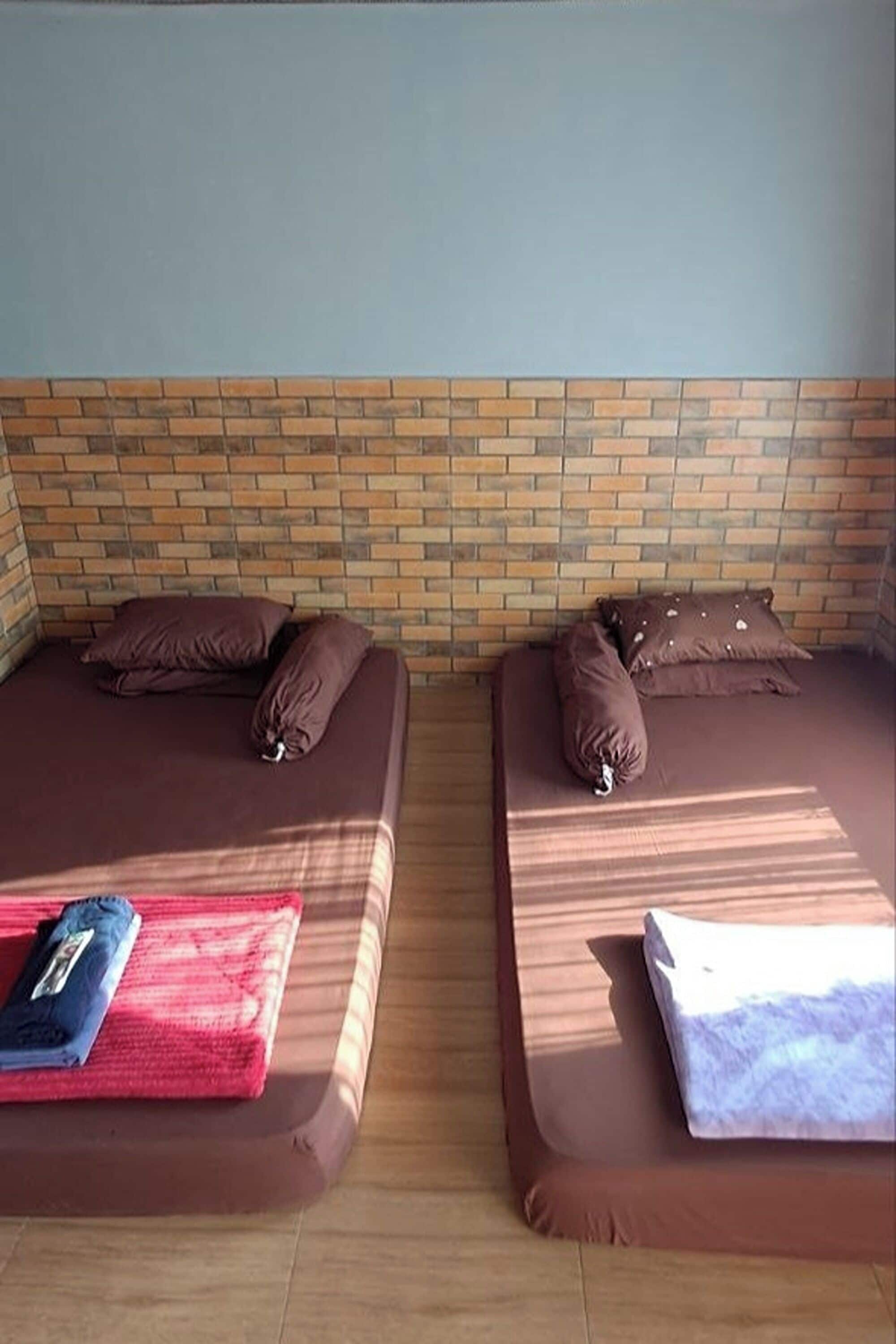 Two single beds with brown bedding and pillows, a red blanket, and a white pillow on a wooden floor.