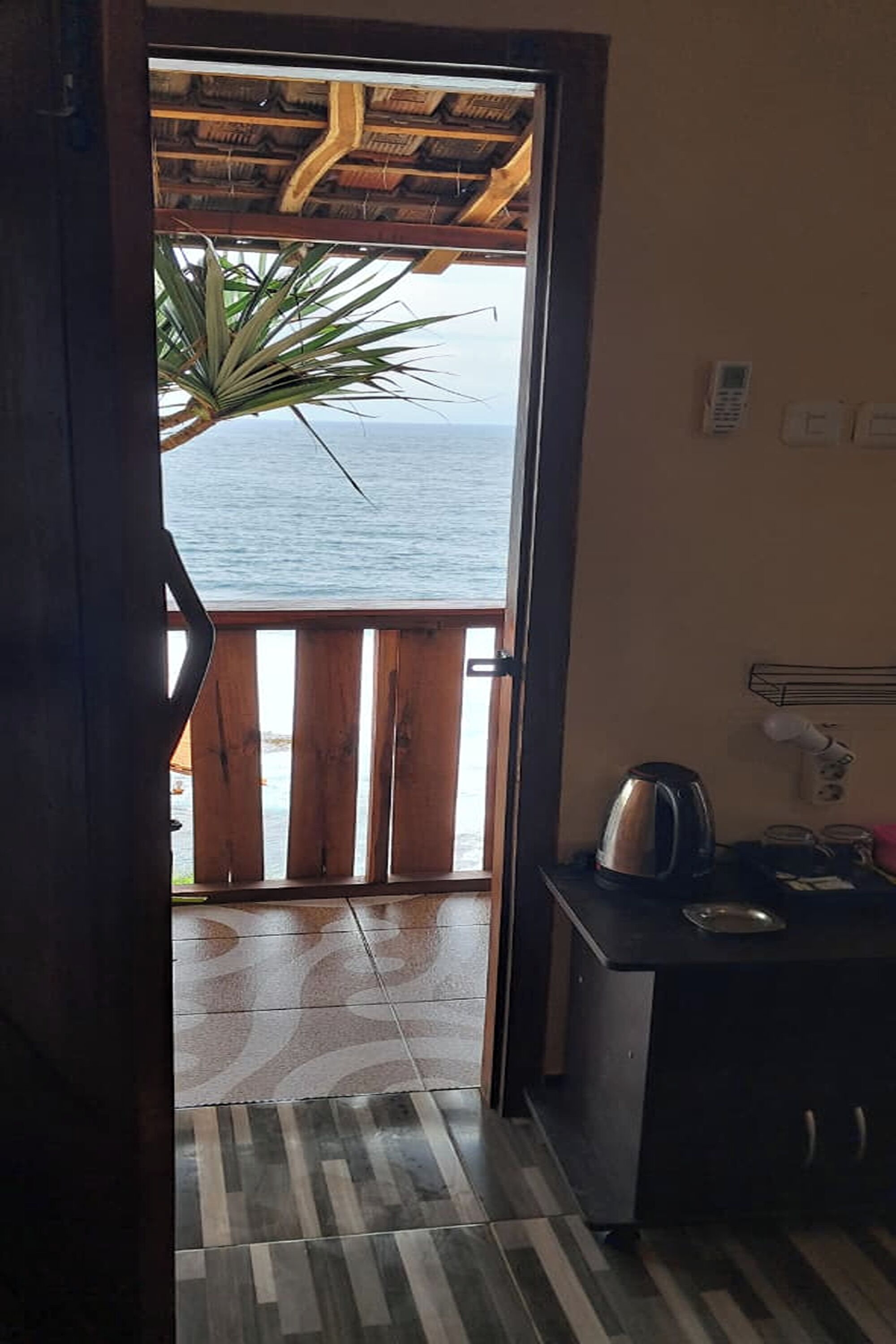 Habitación con vista al mar, balcón de madera, zona de cocina con hervidor y suelo estampado.