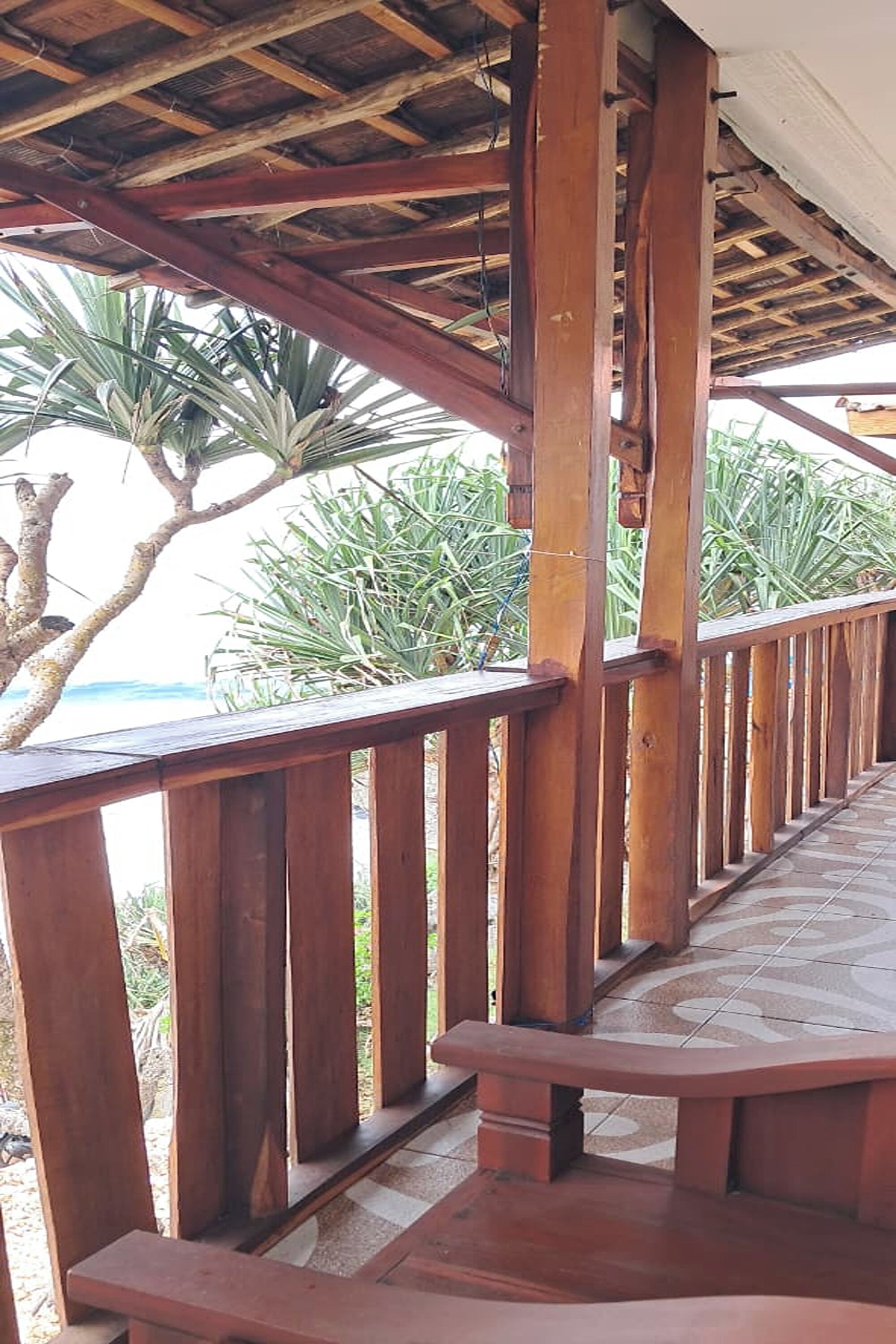 A wooden deck with a tiled floor, surrounded by palm trees and a view of the ocean.