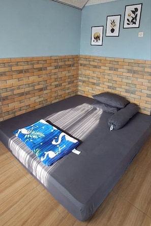 A single bed with a grey mattress and pillows, a blue and white patterned blanket, and a brick-patterned wall.