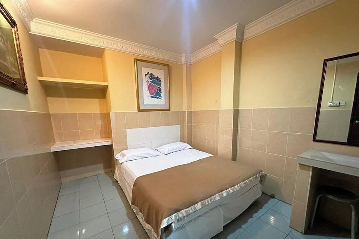Quarto de hotel com cama, mesa de cabeceira, cadeira, espelho e quadro na parede.