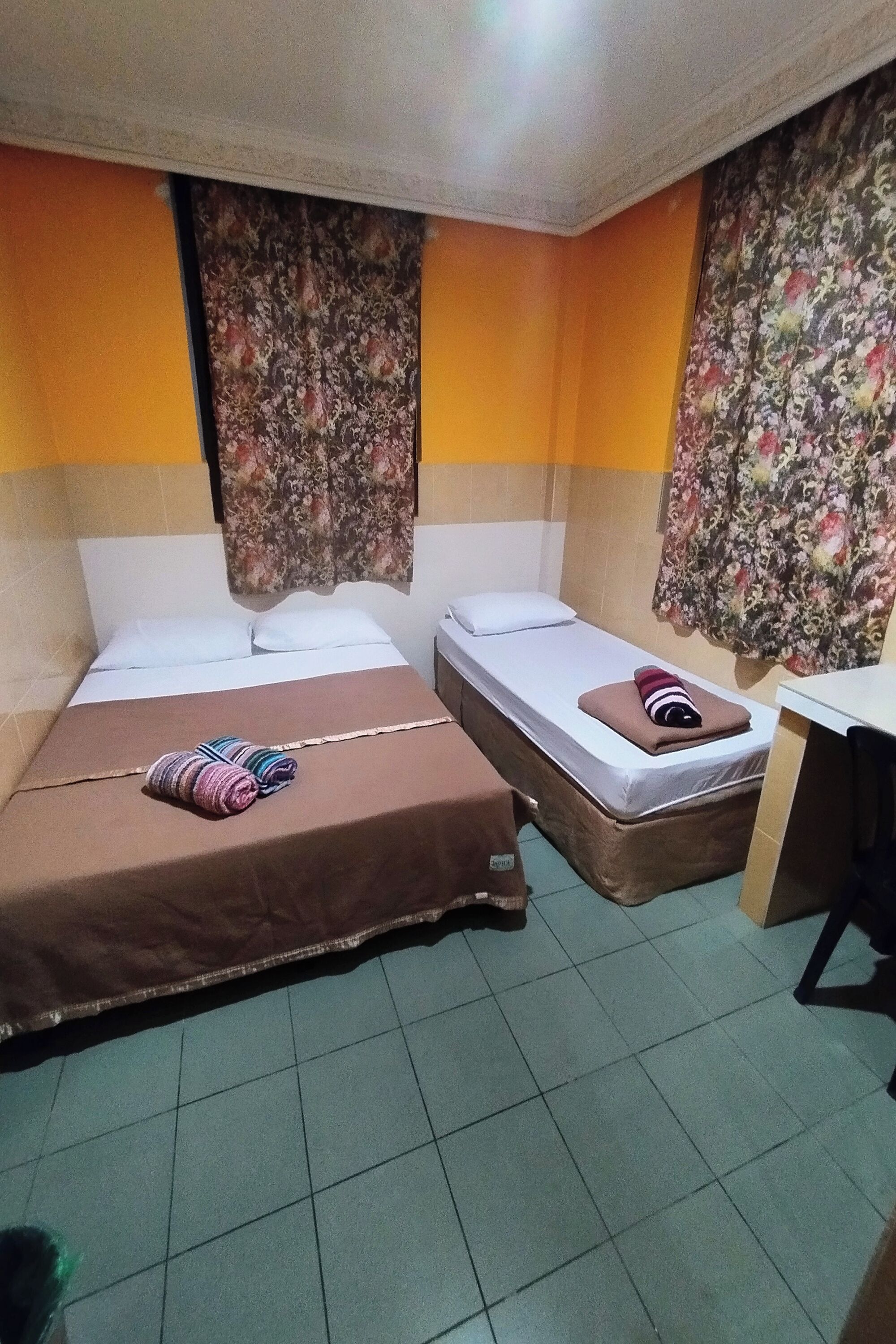 A small, compact room with two single beds, a desk, and a chair.