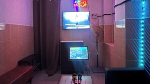 Een karaokezaal met een televisie, een bedieningspaneel, een ventilator en een bank.