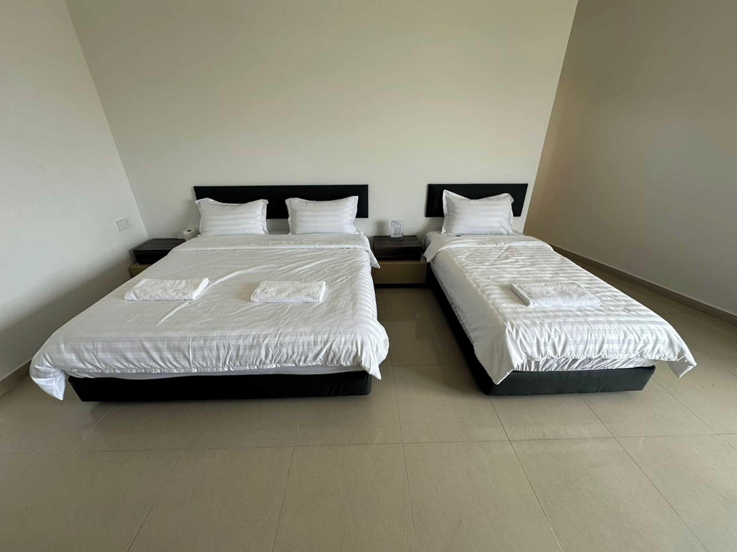 A hotel room with two beds, each with white bedding and pillows, a nightstand, and a small table.