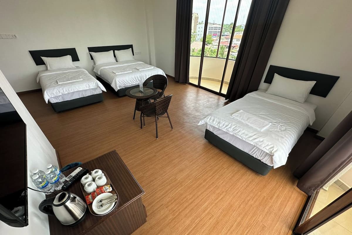 Ett hotellrum med två separata sängar, ett litet bord med en stol och utsikt över staden genom stora fönster.