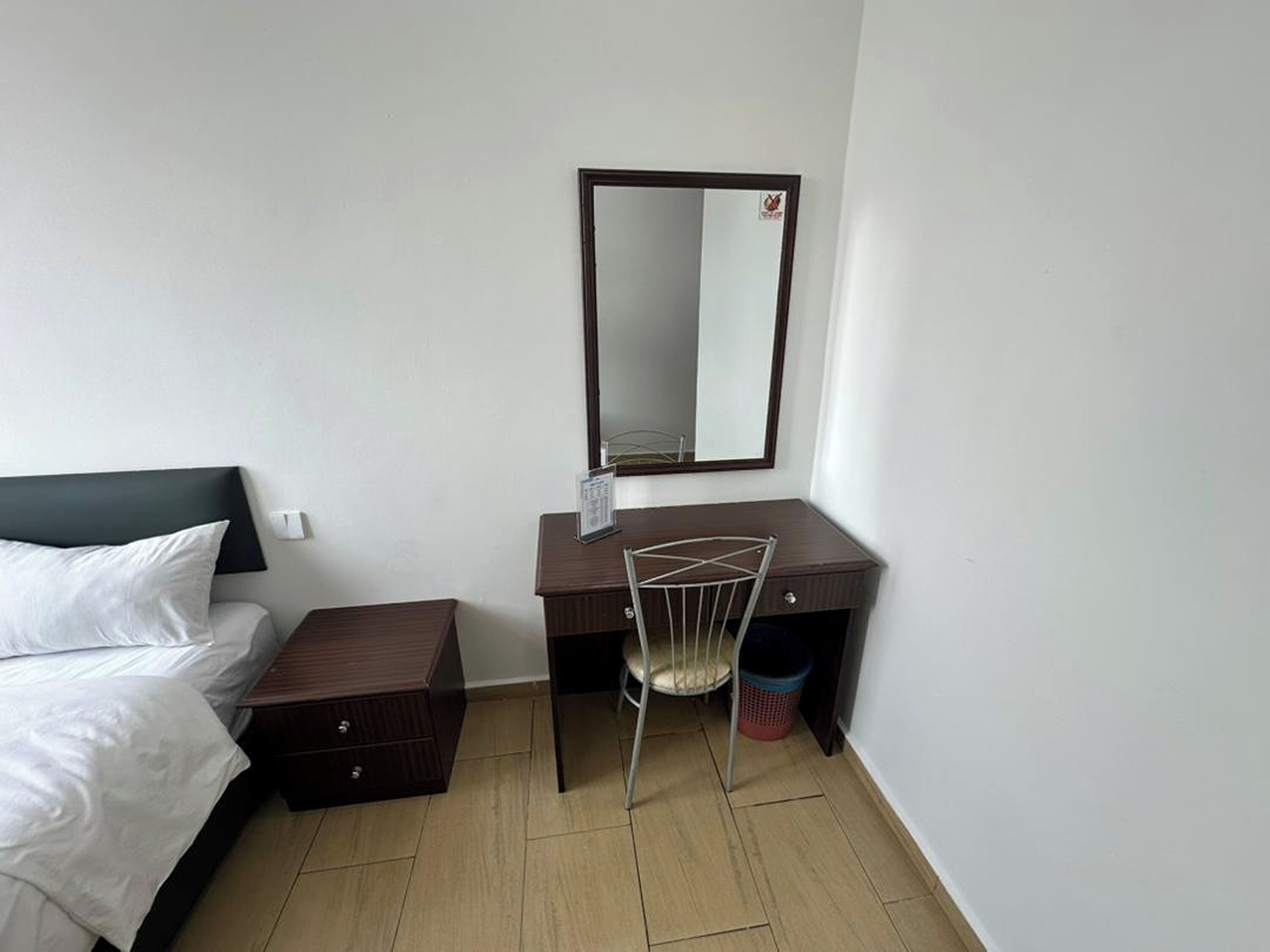 Habitación de hotel con cama, escritorio, silla, espejo y cubo de basura.