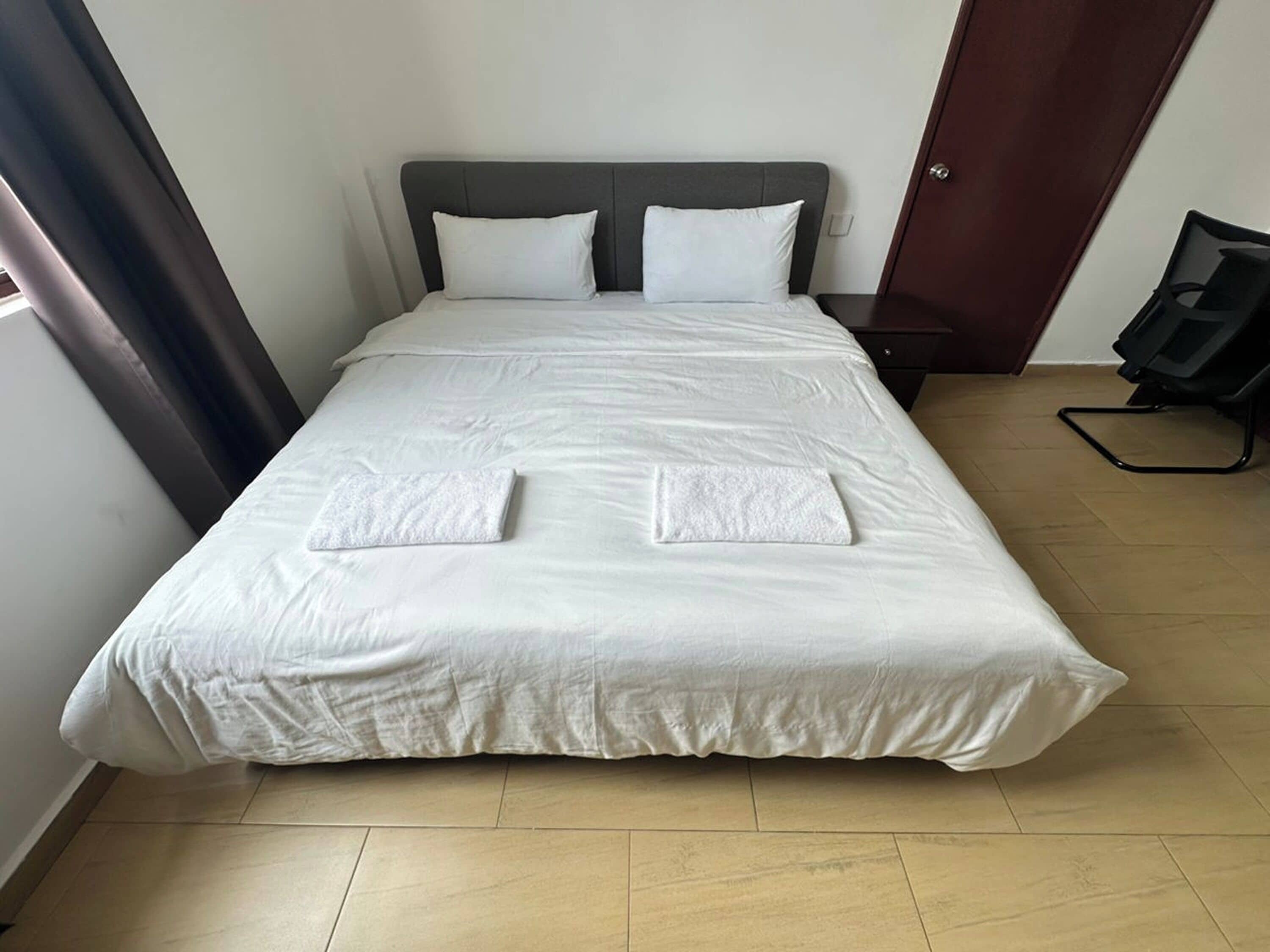 A neatly made bed with white linens and two towels folded at the foot of the bed.