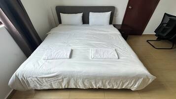 A neatly made bed with white linens and two towels folded at the foot of the bed.