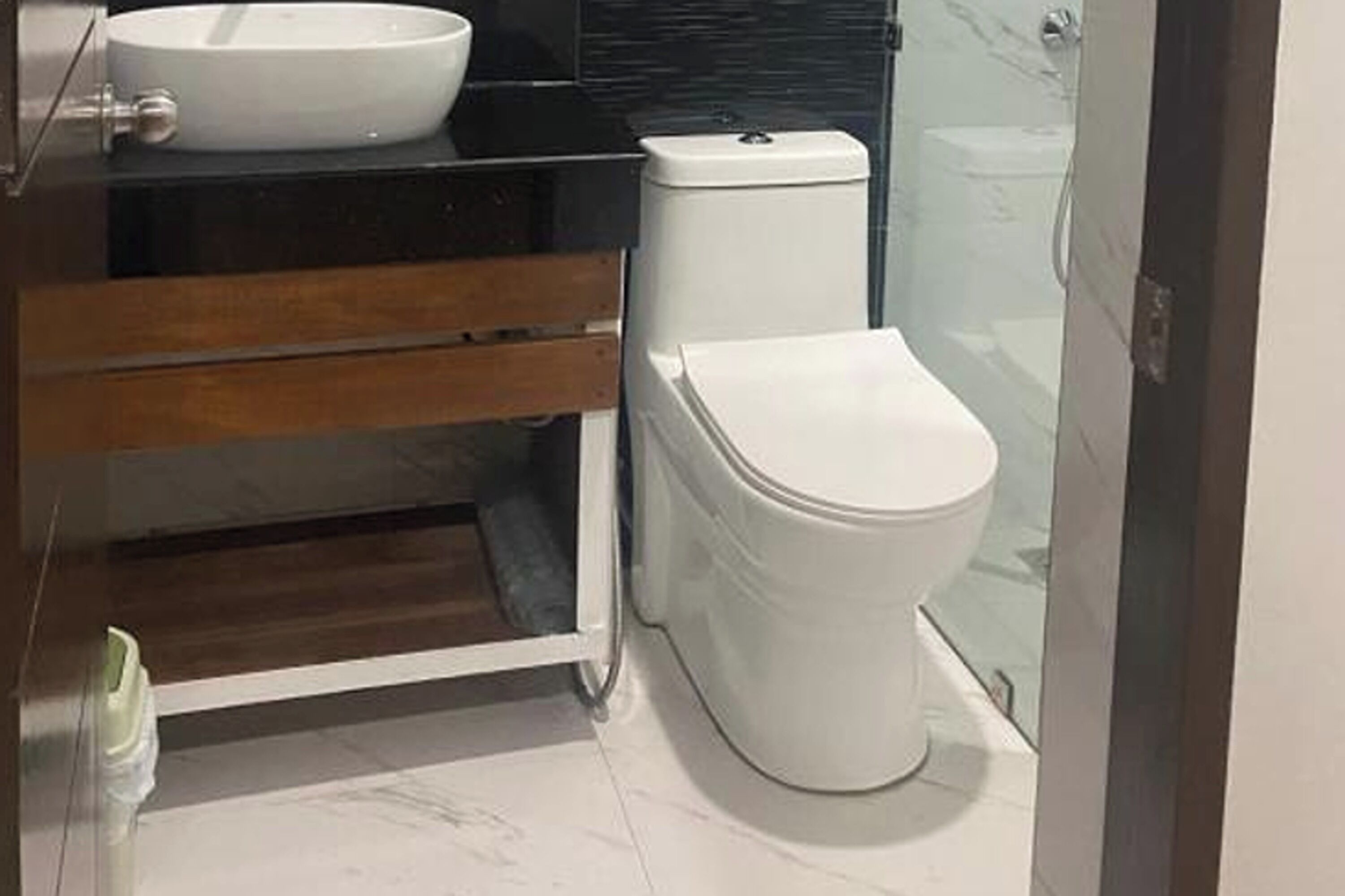 Un baño con lavamanos blanco, encimera negra, mueble de tocador de madera, inodoro blanco y cabina de ducha con mampara de vidrio.