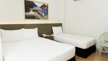 Habitación de hotel con dos camas, un cuadro de un paisaje costero, un equipo de aire acondicionado y una silla de mimbre.