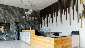 A reception desk with a wooden finish, a marble wall with clocks, and a modern light fixture. - Madison Suites Mactan Cebu (Lapu-Lapu)