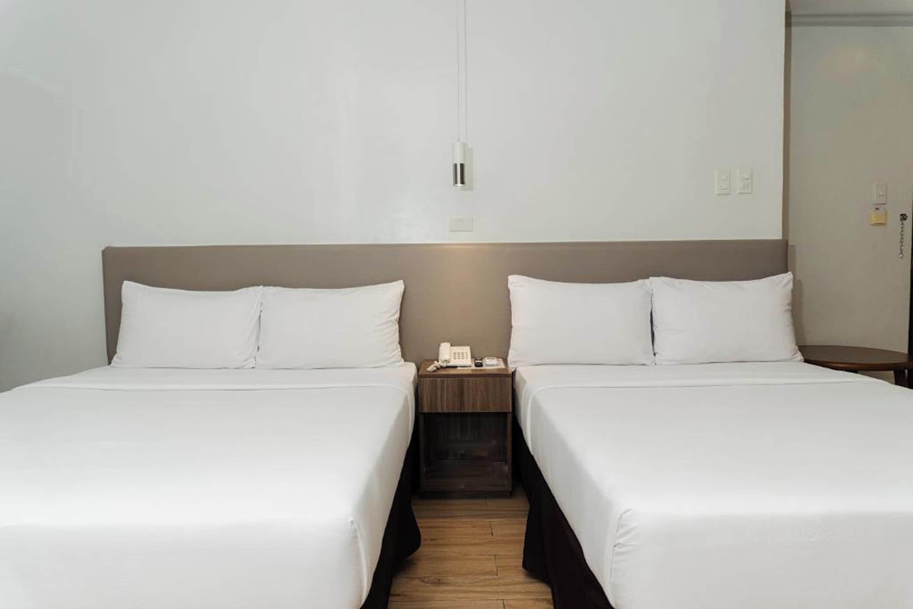 A hotel room with two single beds, a bedside table with a phone, and a hanging light fixture.
