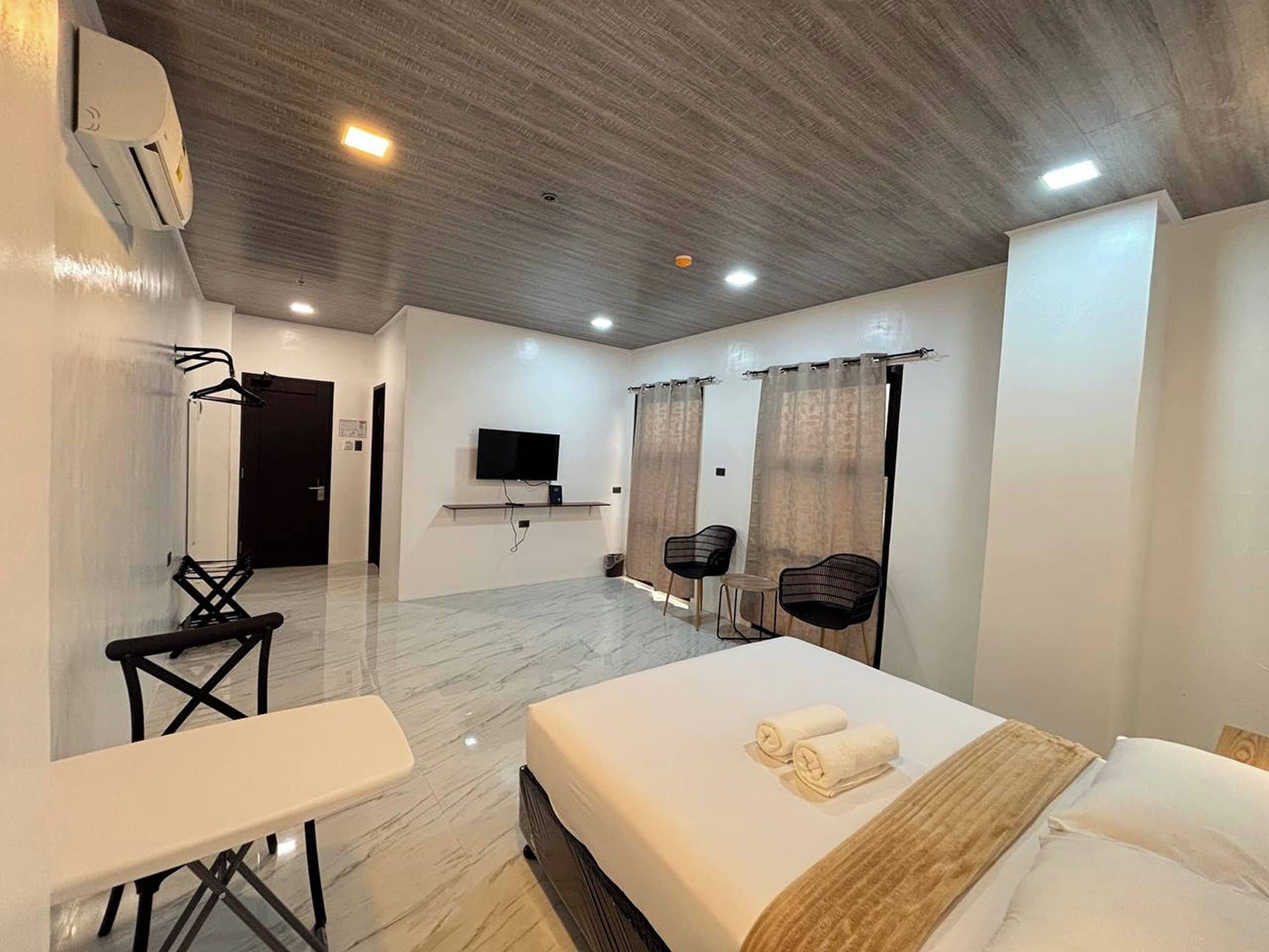 Habitación de hotel moderna con cama, escritorio, dos sillas, televisor y cortinas.