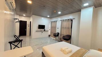 Habitación de hotel moderna con cama, escritorio, dos sillas, televisor y cortinas.