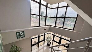 A high-ceilinged room with large windows, a visible fire exit sign, and a staircase leading to an outdoor area. - Hotel De Alexa (Maramag)
