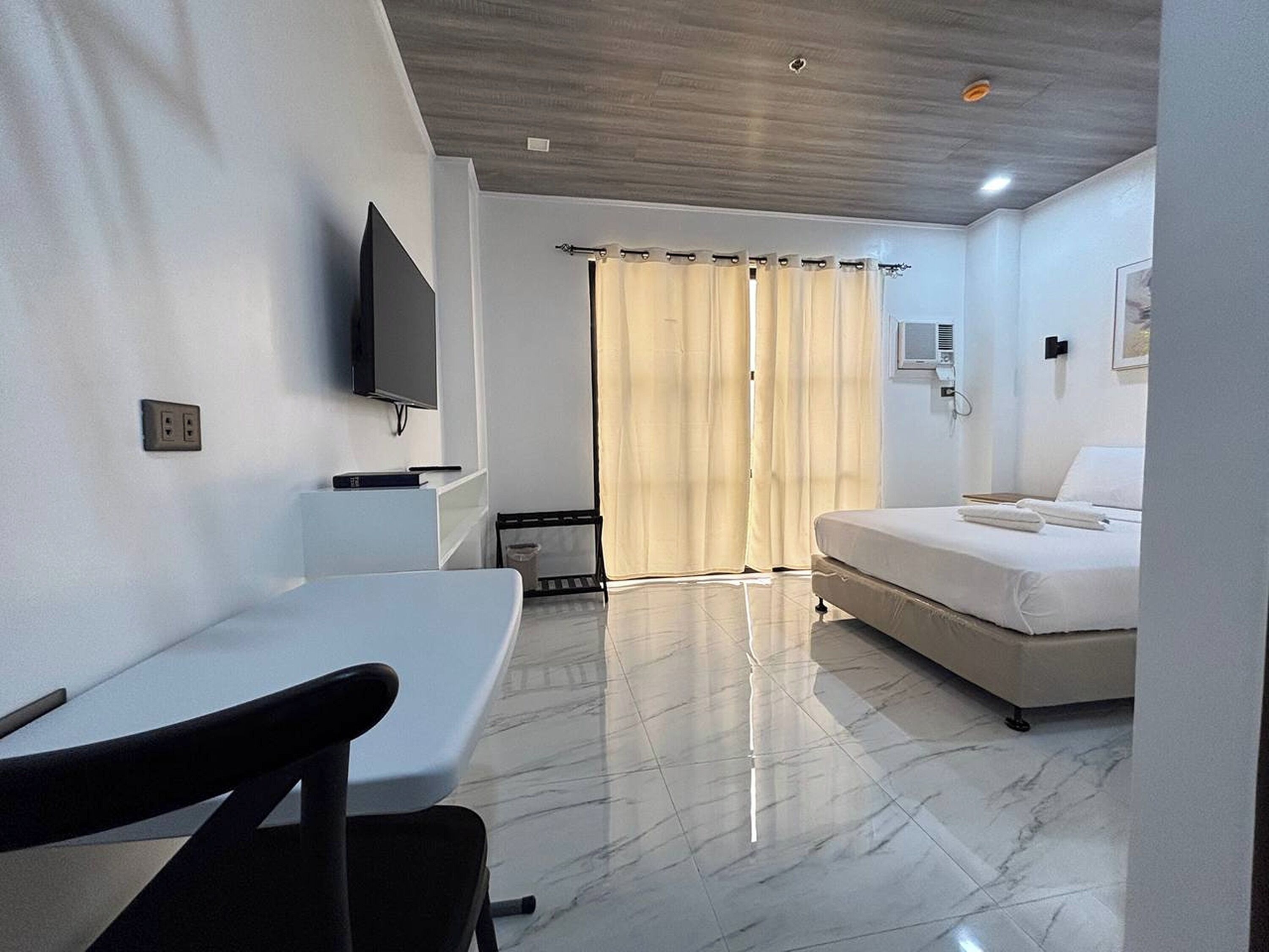 Ein Hotelzimmer mit einem Bett, einem an der Wand befestigten Fernseher, einem Schreibtisch mit Stuhl und einem Badezimmer mit Duschvorhang.