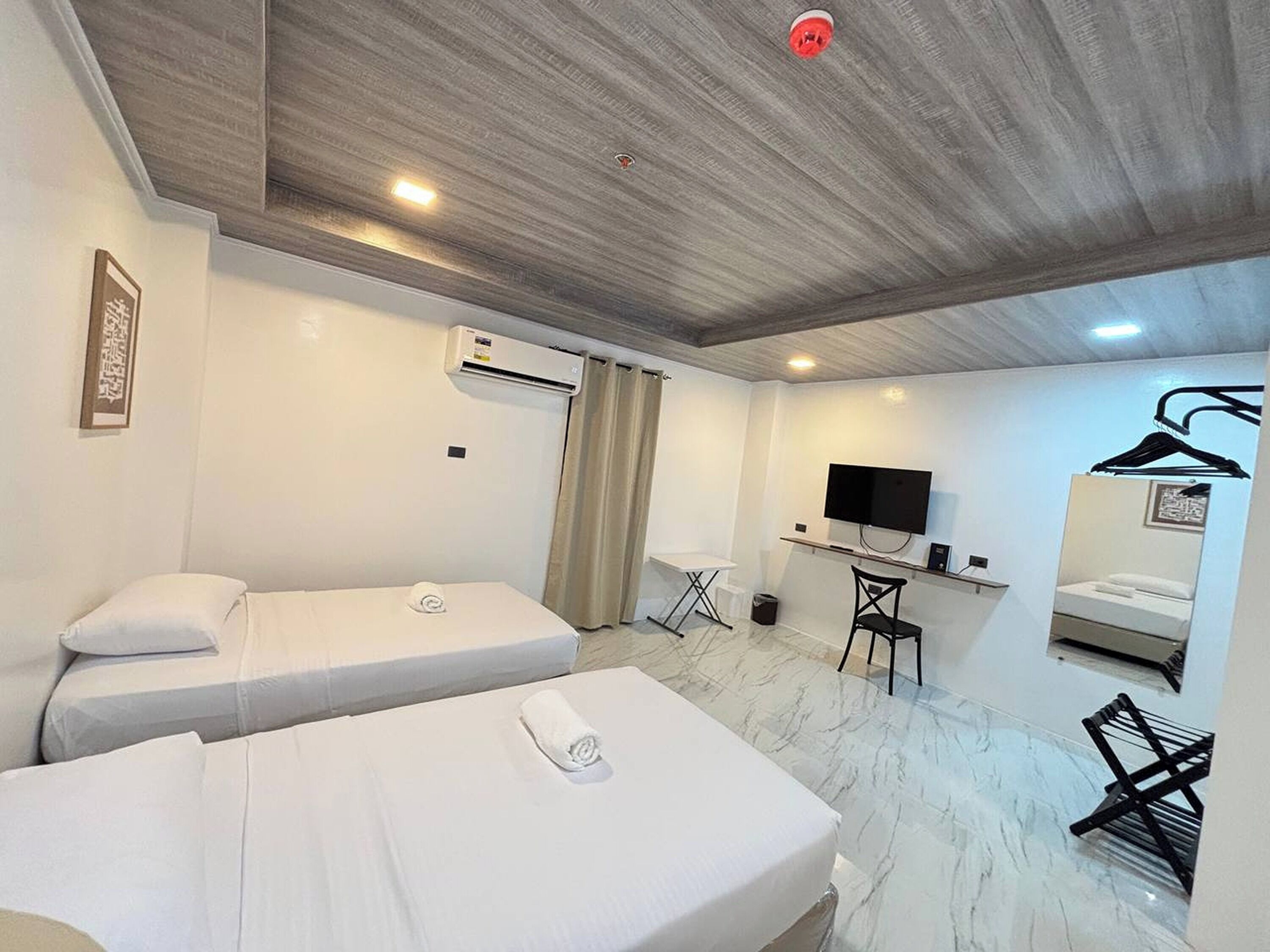Una habitación de hotel con dos camas, un escritorio, un televisor y un espejo.